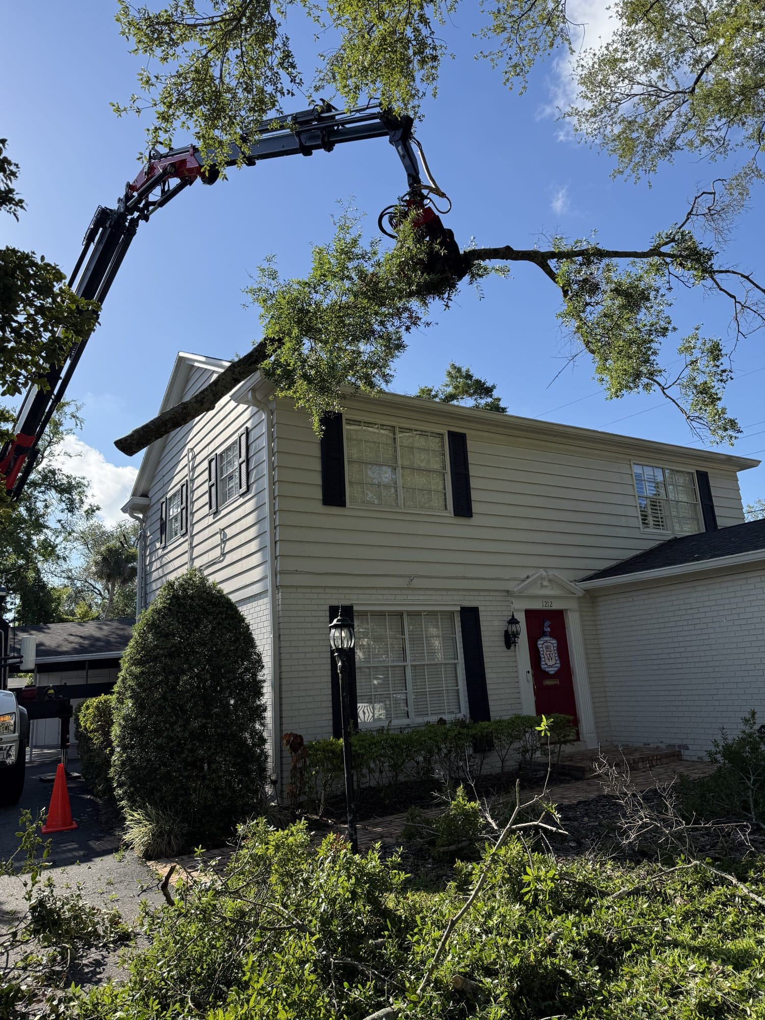 Crane lifting an oak limb over a two-story Tampa home
